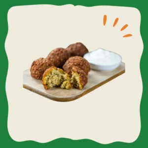 Cinco falafels sobre una tabla de picar, uno está cortado a la mitad y se ve su relleno, hay una crema agria como acompañante